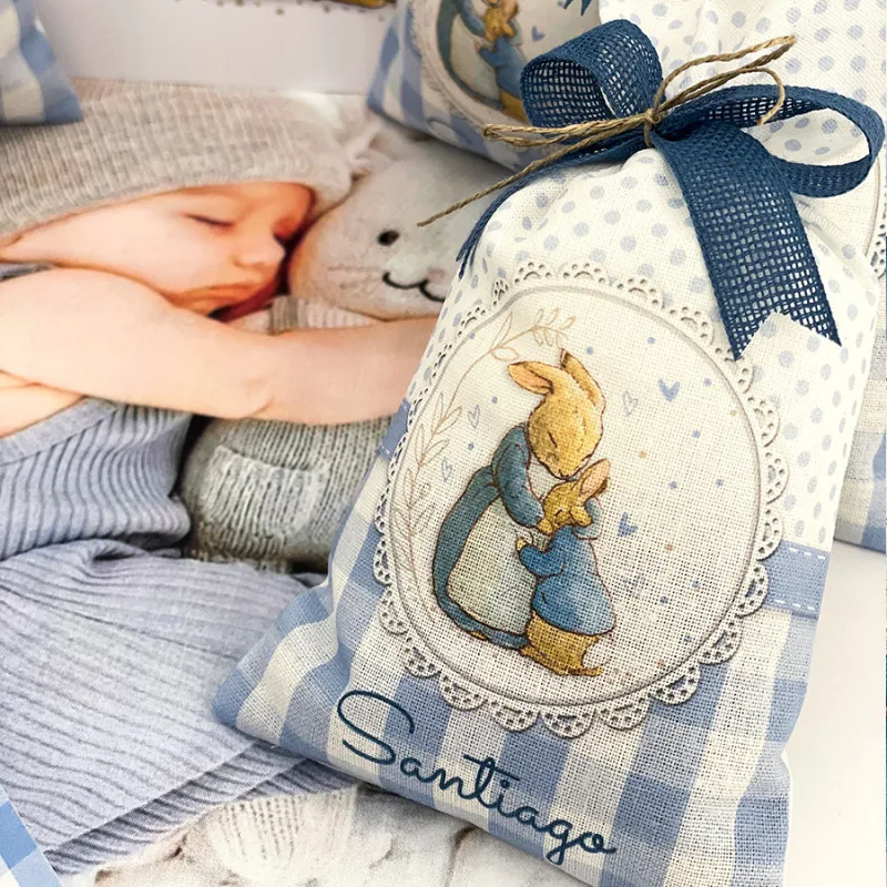 Sacchettino a quadretti azzurri con illustrazione e nome del bambino stampati, accanto a un neonato che dorme